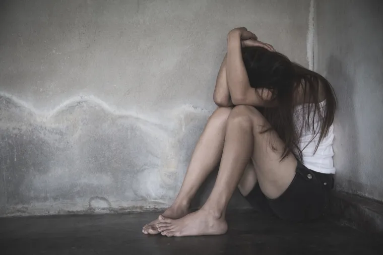 A young woman hugs her head defensively in a corner